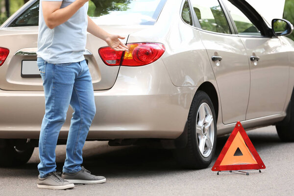 Man calling his insurance agent while standing near broken car on road