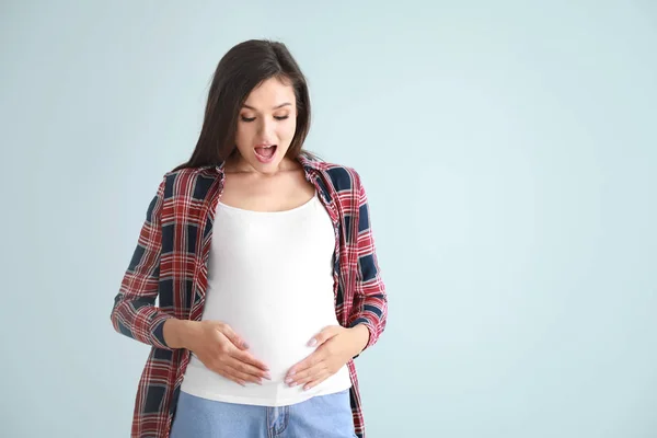 Здивована вагітна жінка на кольоровому фоні — стокове фото