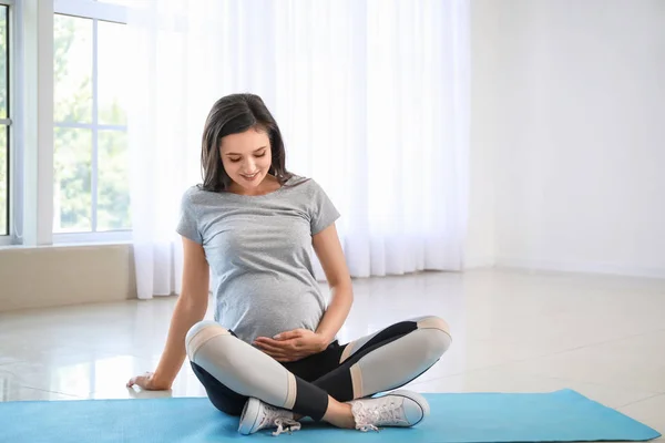 Pregnant woman in sportswear sitting on yoga mat at home — Stock Photo, Image
