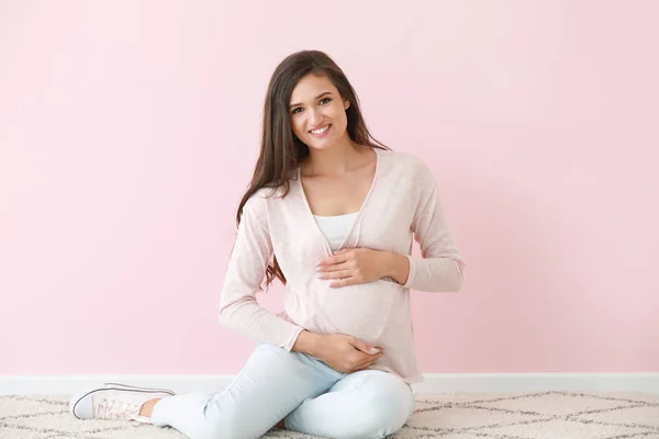 Jonge zwangere vrouw zittend in de buurt van kleur muur — Stockfoto