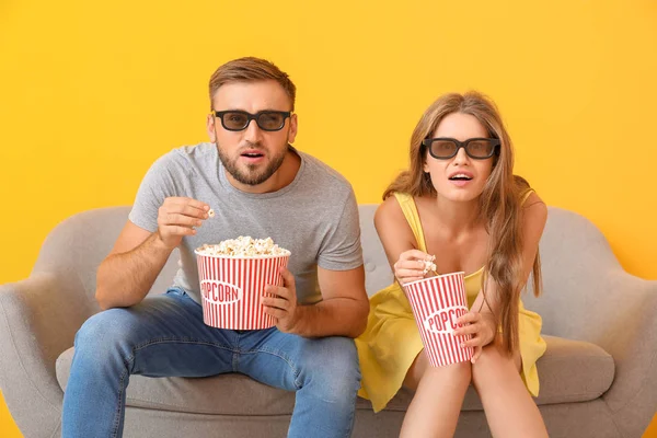 Young couple with popcorn watching movie on sofa against color background — Stock Photo, Image