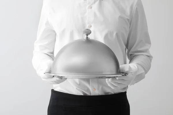 Handsome waiter with tray and cloche on light background, closeup — Stock Photo, Image