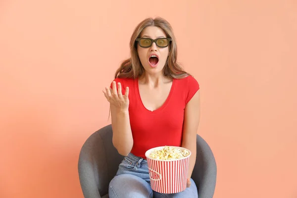 Shocked woman with popcorn watching movie on color background — Stock Photo, Image