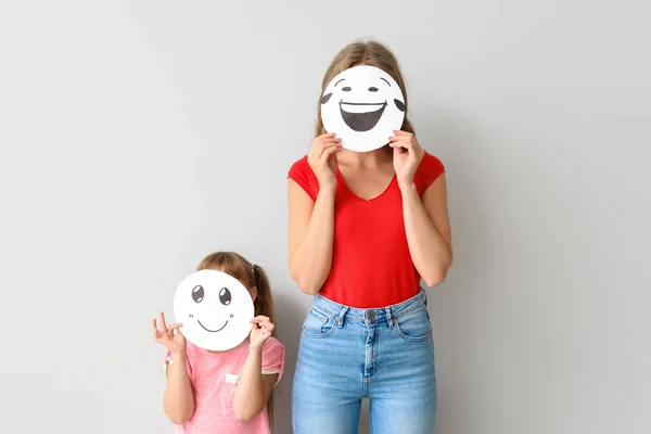 Madre e hija pequeña escondiendo caras detrás de emoticonos contra fondo claro — Foto de Stock