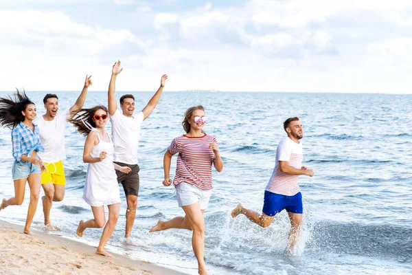 Glada vänner som springer på stranden på orten — Stockfoto