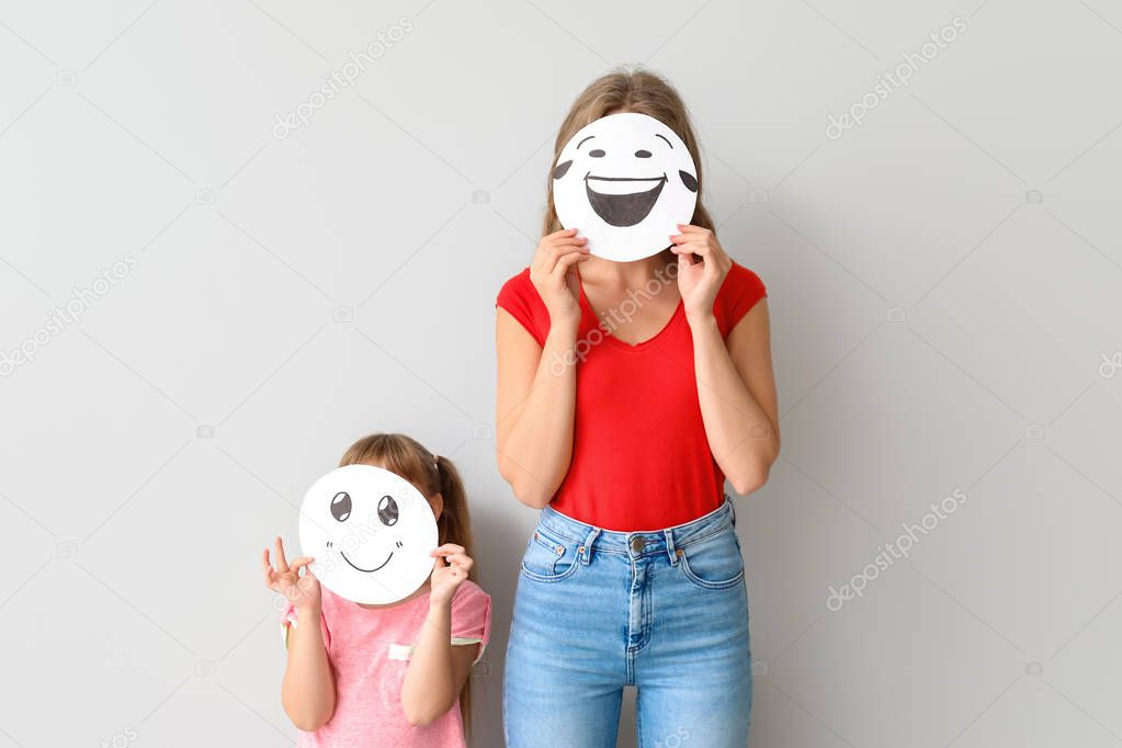 Mother and little daughter hiding faces behind emoticons against light background