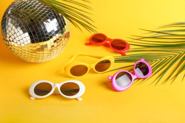 Renk arka plan üzerinde disko topu ve tropikal yaprakları ile farklı şık güneş gözlüğü