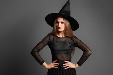 Gri arka planda Cadılar Bayramı için cadı gibi giyinmiş güzel kadın