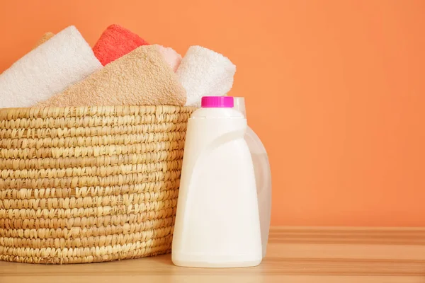 Basket with clean towels and washing agents on table near color wall — Stock Photo, Image