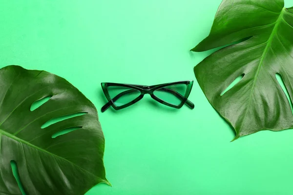 Stylish eyeglasses with tropical leaves on color background — Stock Photo, Image