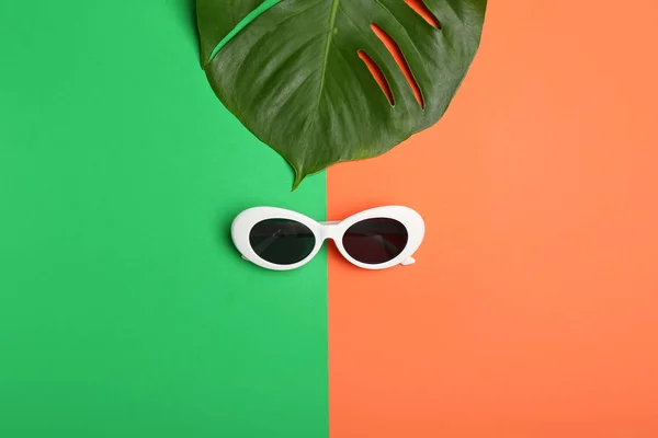 Stylish sunglasses with tropical leaf on color background — Stock Photo, Image