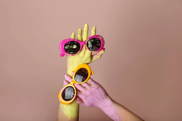 Painted female hands with stylish sunglasses on color background — Stock Photo, Image