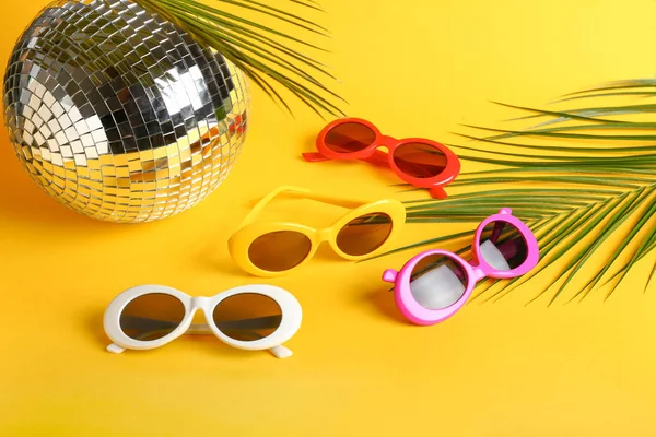 不同的时尚太阳镜与迪斯科球和热带叶子的颜色背景 — 图库照片