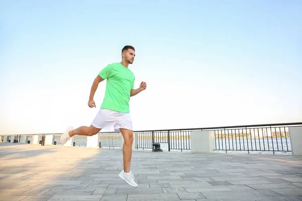 Handsome sporty man running near river — Stock Photo, Image