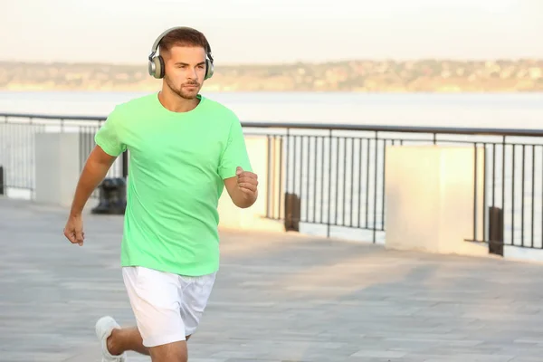 Handsome sporty man listening to music and running outdoors — Stock Photo, Image
