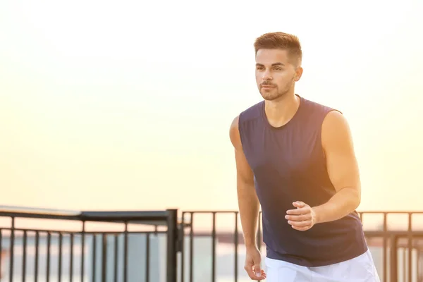 Handsome sporty man running near river — Stock Photo, Image