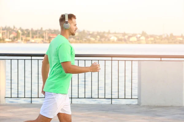 Handsome sporty man listening to music and running outdoors — Stock Photo, Image