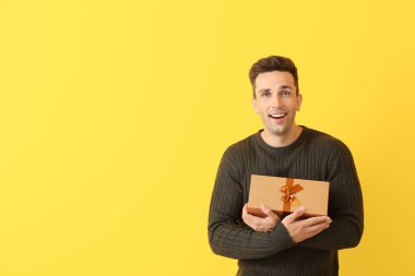 Handsome young man with gift on color background
