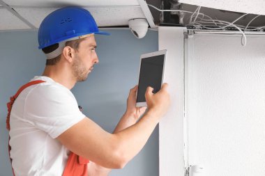 Electrician with tablet computer installing alarm system indoors clipart