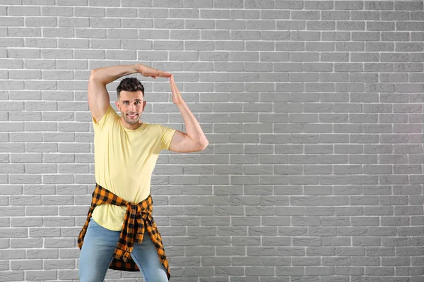 Handsome young man dancing against brick wall — Stock Photo, Image