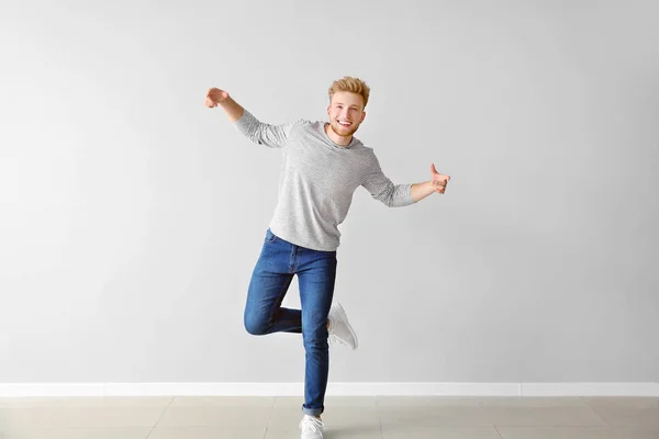 Handsome young man dancing against light wall — Stock Photo, Image
