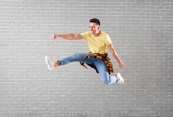 Handsome young man jumping against brick wall — Stock Photo, Image