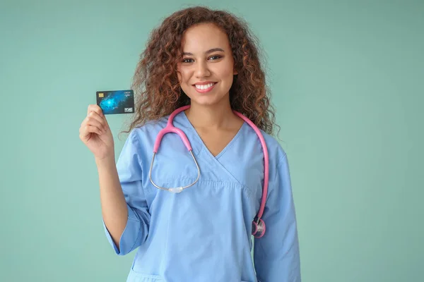 African-American doctor with credit card on color background