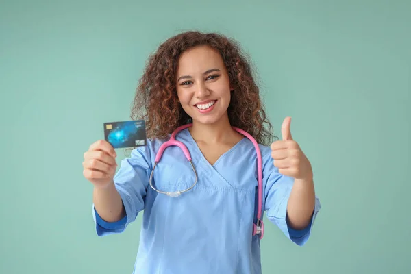 Médico afro-americano com cartão de crédito mostrando polegar para cima em fundo de cor — Fotografia de Stock