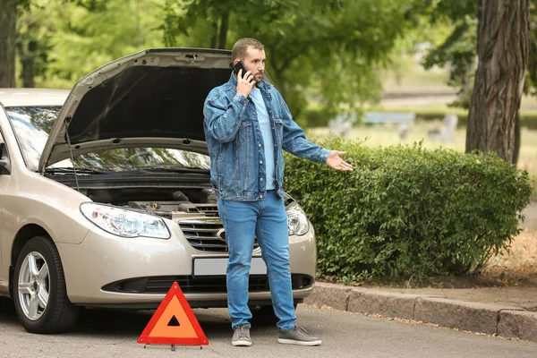 Чоловік викликає свого страхового агента, стоячи біля розбитого автомобіля на дорозі — стокове фото