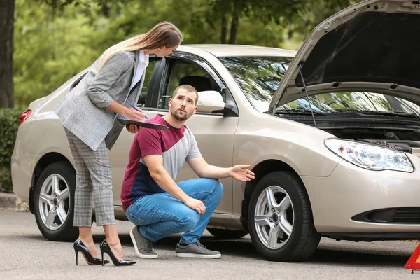 Hombre joven y agente de seguros cerca de coche dañado al aire libre — Foto de Stock