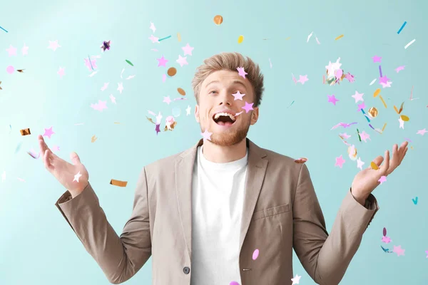 Glücklicher junger Mann und fallendes Konfetti auf farbigem Hintergrund — Stockfoto
