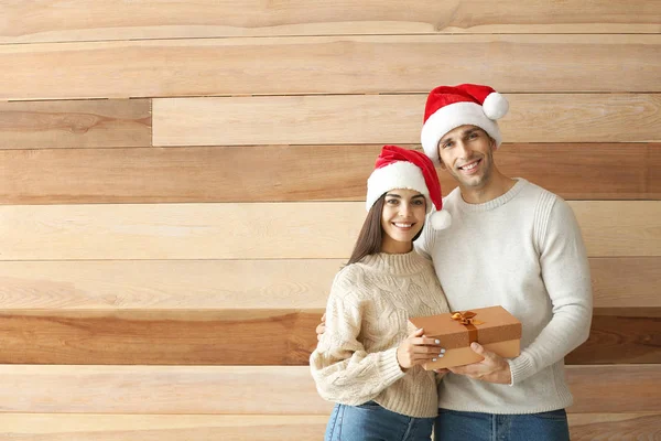 Happy young couple with Christmas gift on wooden background — Stock Photo, Image