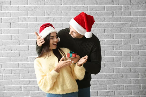 Homem dando sua namorada presente de Natal contra parede de tijolo — Fotografia de Stock