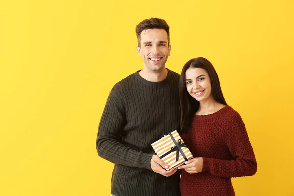 Feliz pareja joven con el regalo en el fondo de color — Foto de Stock