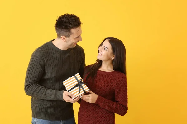 Happy young couple with gift on color background — Stock Photo, Image