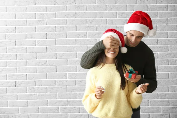 Homem dando sua namorada presente de Natal contra parede de tijolo — Fotografia de Stock