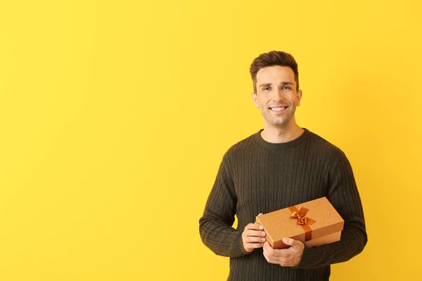 Handsome young man with gift on color background — Stock Photo, Image