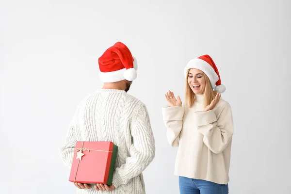 Man hiding Christmas gift for his wife behind back on light background — Stock Photo, Image