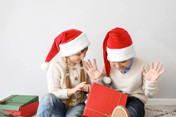 Happy children with Christmas gifts sitting near light wall — Stock Photo, Image