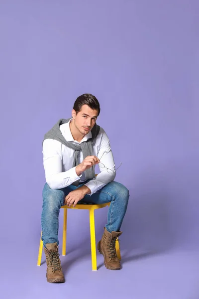 Fashionable man sitting on chair against color background — Stock Photo, Image