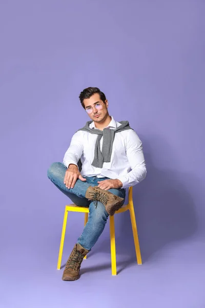色の背景に対して椅子に座っているファッショナブルな男 — ストック写真