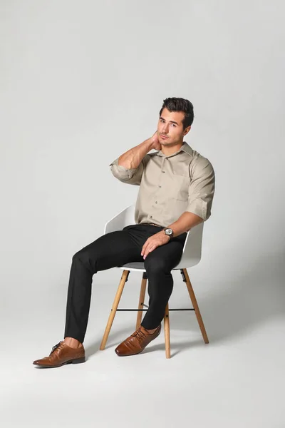 Fashionable man sitting on chair against light background — Stock Photo, Image