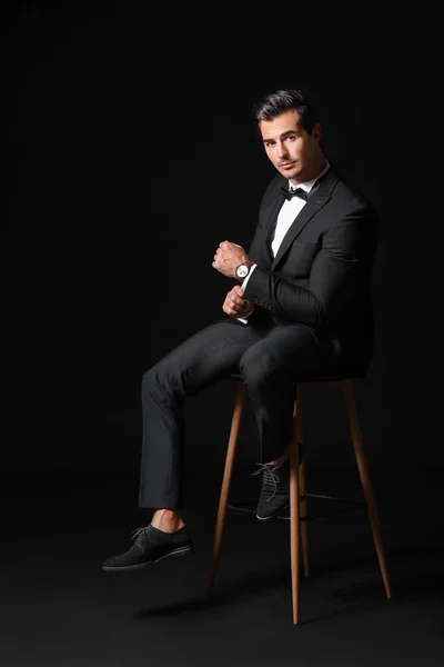 Fashionable man in formal clothes sitting on chair against dark background — Stock Photo, Image