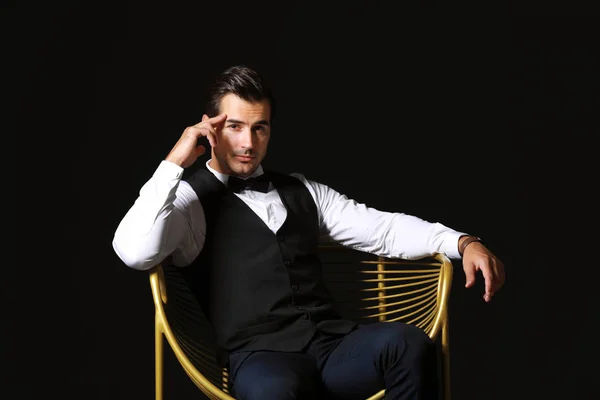Modny człowiek siedzi w fotelu na ciemnym tle — Zdjęcie stockowe