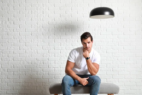 Стильний модний чоловік сидить на лавці біля білої цегляної стіни — стокове фото