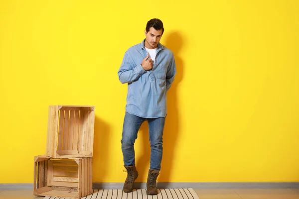 Stylish fashionable man and wooden boxes against color wall — Stock Photo, Image