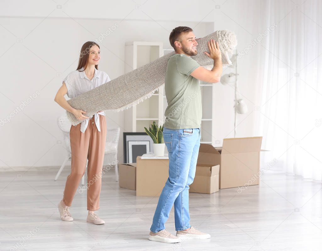 Young couple carrying carpet after moving into new house