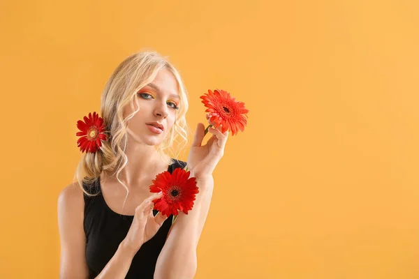 Piękna młoda kobieta z kwiatami Gerbera na kolorowym tle — Zdjęcie stockowe