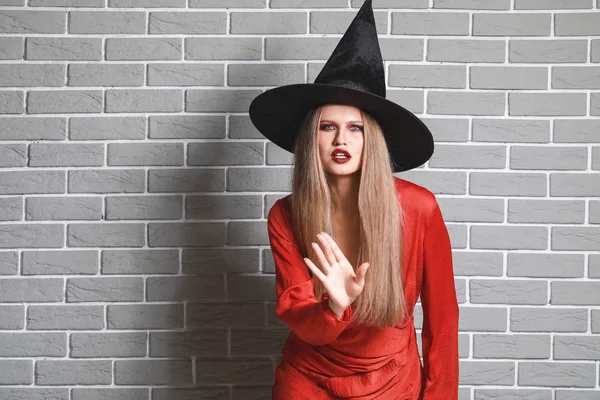 Hermosa mujer vestida de bruja para Halloween contra la pared de ladrillo —  Fotos de Stock