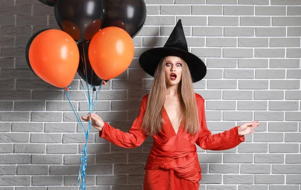 Mulher bonita vestida como bruxa para o Halloween contra a parede de tijolo — Fotografia de Stock